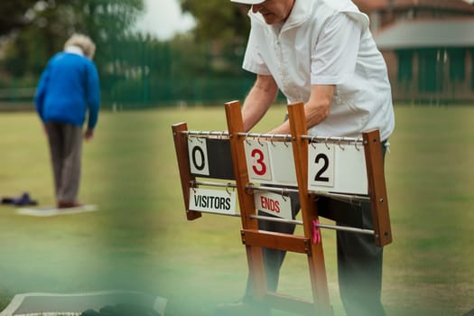 A senior man at a bowling green setting up the scoreboard.