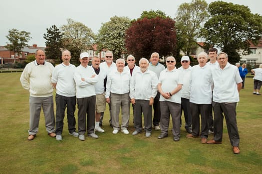A front view shot of a community of senior men smiling at a bowling green.