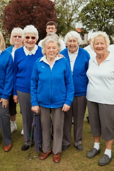 A front view shot of senior friends standing at a bowling green smiling at the camera.