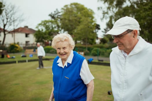 A front view shot of a senior couple smiling at a bowling green.