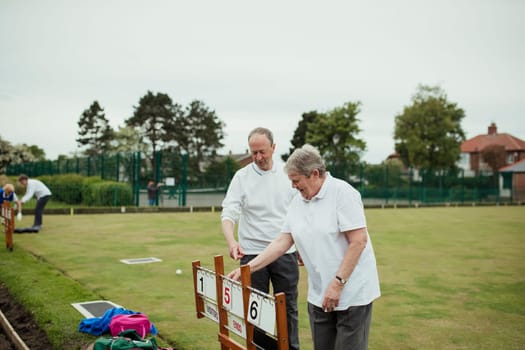 Two seniors at a bowling green setting up the scoreboard.