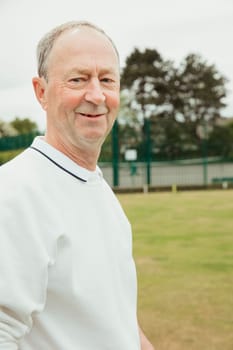 A portrait of a senior man smiling at a bowling green.