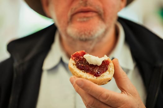 A close up shot of a bitten jam scone, held by a senior man.