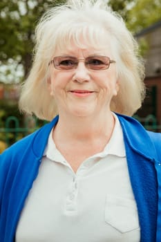 A portrait of a senior woman smiling at a bowling green. She is wearing glasses.