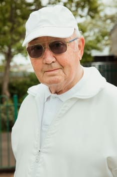 A portrait of a senior man smiling at a bowling green. He is wearing sunglasses.