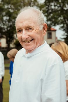 A portrait of a senior man smiling at a bowling green.