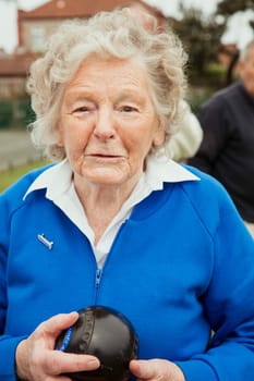 A portrait of a senior woman at a bowling green, holdng a bocce ball.