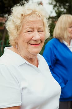 A portrait of a senior woman smiling at a bowling green.