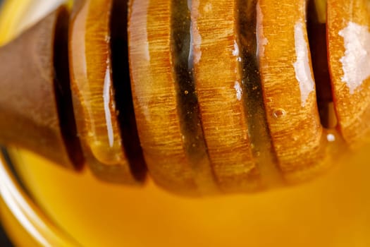 Honey in a glass bowl and a wooden stick for honey on a dark background