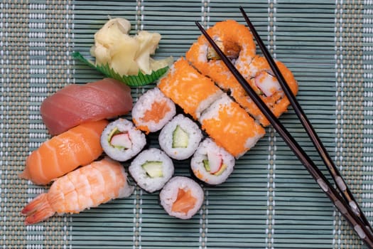 Traditional japanese sushi menu. Close-up of various kinds of sushi rolls with salmon, sashimi and other slices of raw fish and a pair of wooden chopsticks served on a green bamboo mat. Macro. Top view.