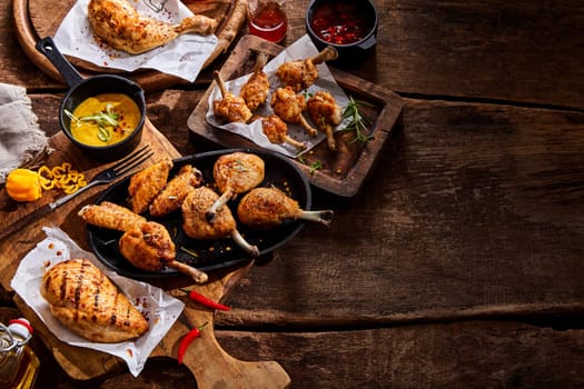 Assorted grilled chicken portions on a buffet table at a summer BBQ seasoned with hot chili pepper and fresh herbs and served with mustard dip, top down with copy space