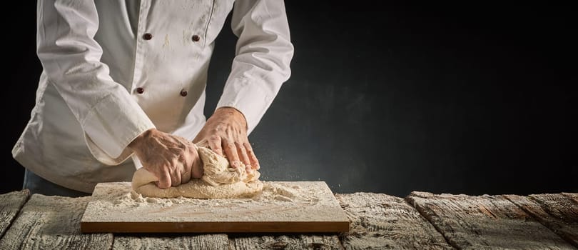 Hands of a chef or baker kneading raw dough on an old wooden board in a rustic panorama banner with copy space