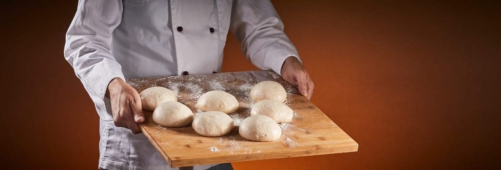 Chef carrying portions of raw dough on a board in a pizzeria ready for making Italian pizzas in a panorama banner with copy space