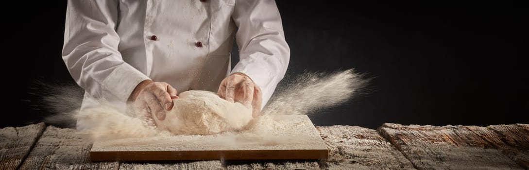 Freeze motion explosion of cooking flour as a chef or cook works on a mound of raw dough in a vintage table in a rustic panorama banner with copy space