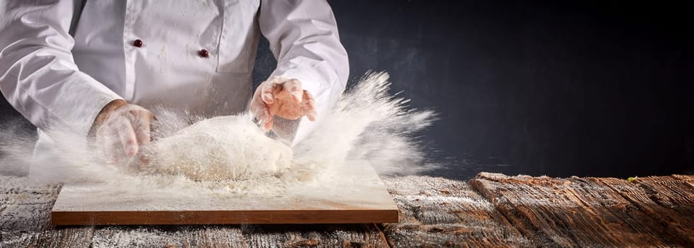 Freeze motion of an explosion of flour as a baker or chef prepares a mound of dough for cooking on a wooden board in a rustic panorama banner with copy space