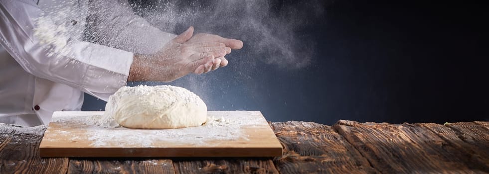 Chef or baker dusting a heap of uncooked dough with flour suspended in the air by clapping his hands in a rustic panorama banner with copy space