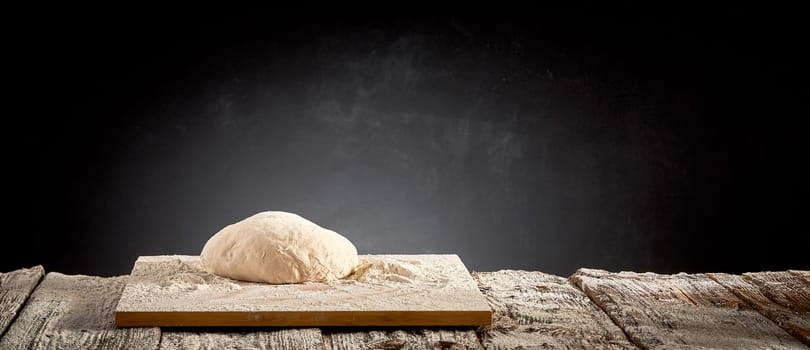 Large mound of raw dough on a floured cutting board on an old rustic or vintage kitchen table in a rustic panorama banner with copy space