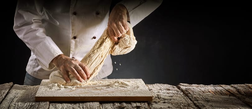Baker or chef stretching a portion of raw dough as he works on it during preparation for cooking in a rustic panorama banner with copy space