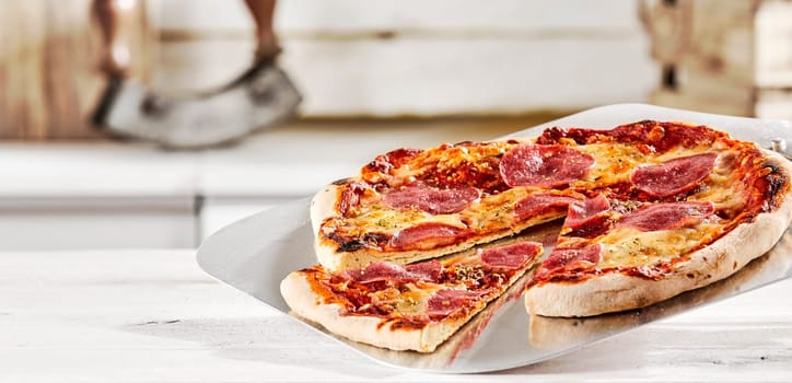 Traditional salami pizza on a metal paddle in a pizzeria with a single wedge cut from the whole in a panorama banner for menu or advertising