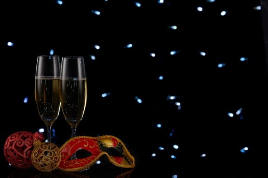 Two wineglasses with champagne and Christmas decorations on a black background with LED lights garland. Copy space. New Year and Christmas