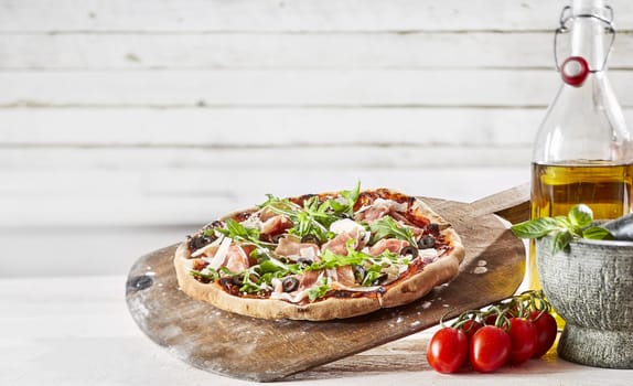 Speciality oven-fired prosciutto Italian pizza with fresh rocket parmesan cheese on a crispy crust on an old wooden paddle with fresh ingredients, copy space above for menu advertising