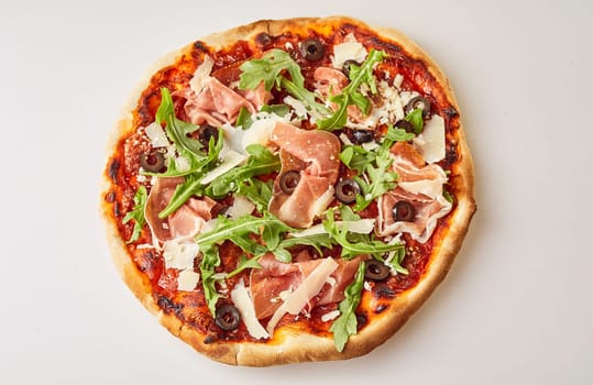 Oven-fired prosciutto, rocket and olive Italian pizza on a crispy pastry base with parmesan cheese topping viewed whole from above