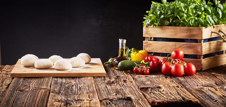 Fresh ingredients for Italian vegetarian pizzas with individual portions of raw dough on a tray, basil, tomatoes, sweet pepper, brinjal, and courgette in a panorama banner with copy space