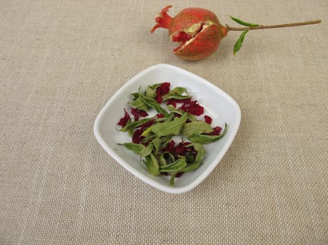 A small pomegranate, pomegranate leaves and pomegranate blossoms in a bowl