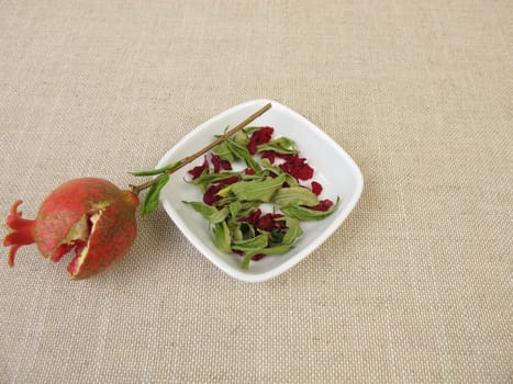 A small pomegranate, pomegranate leaves and pomegranate blossoms in a bowl