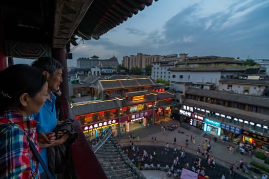 Xian, China -  July 2019 : Chinese senior tourists watching the bustling streets of the Muslim Quarter in the evening from the viewpoint balcony in Drum Tower, Xian city, Shaanxi Province