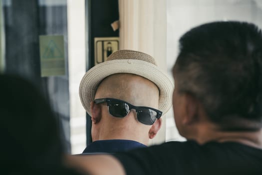 Xian, China -  July 2019 : A chinese man wearing his sunglasses on the back of his shaved head with a hat that gives the illusion of a face, public transport