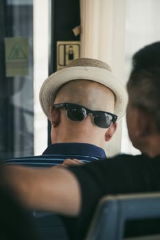Xian, China -  July 2019 : A chinese man wearing his sunglasses on the back of his shaved head with a hat that gives the illusion of a face, public transport