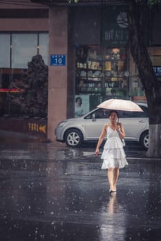 Chengdu, China -  July 2019 : Beautiful Chinese woman in a bridal white dress walking with an umbrella during tropical monsoon rain