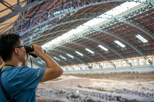Xian, China -  July 2019 : Chinese tourist looking through the binoculars at the Terracota Army, Xian, Shaanxi Province
