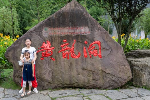 Wullingyuan, China -  August 2019 : Children posing for a picture in front of a large boulder with chinese characters written in red on it,  Hunan Province