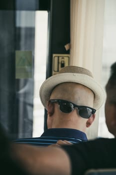 Xian, China -  July 2019 : A chinese man wearing his sunglasses on the back of his shaved head with a hat that gives the illusion of a face, public transport