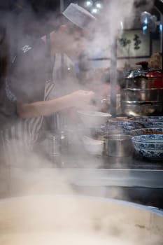 Xian, China -  August 2019 : Chinese chef preparing hot food on a food stall operating at night on the street in the Muslim Quarter