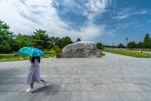 Xian, China -  July 2019 : Woman with an umbrella walking in front of large boulder on the site of Mausoleum of the First Qin Emperor, creator of the Terracota Army, Shaanxi Province