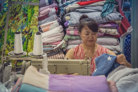 Chengdu, China -  July 2019 : Chinese woman uses electric sewing machine for sewing clothes in her textile shop