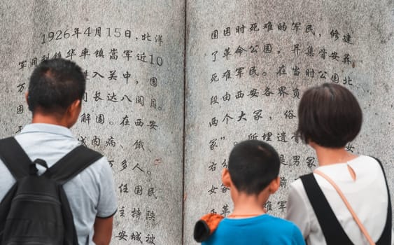 Xian, China -  August 2019 : Family reading text from a page in a large sculpture stone book in Geming Revolution Park, Shaanxi Province