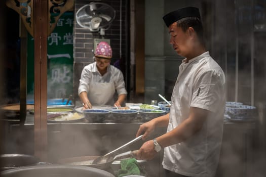 Xian, China -  August 2019 :  Chinese chef preparing hot food on a food stall operating at night on the street in the Muslim Quarter