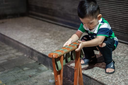 Xian, China -  August 2019 : Cute little chinese boy playing with folding chair outside small local bakery on the street in Muslim Quarter