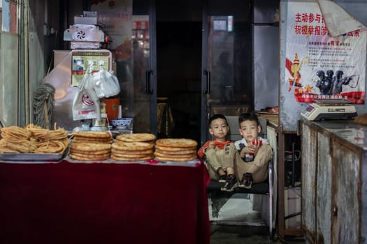Xian, China -  August 2019 :  Two little boys playing games on a small mobile device while sitting on chairs in a small local bakery on the street in Muslim Quarter