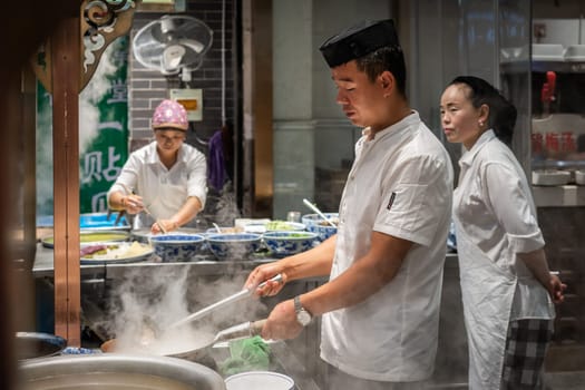 Xian, China -  August 2019 : Chinese chef preparing hot food on a food stall operating at night on the street in the Muslim Quarter