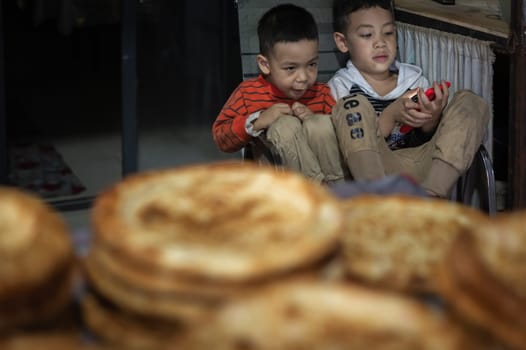 Xian, China -  August 2019 :  Two little boys playing games on a small mobile device while sitting on chairs in a small local bakery on the street in Muslim Quarter