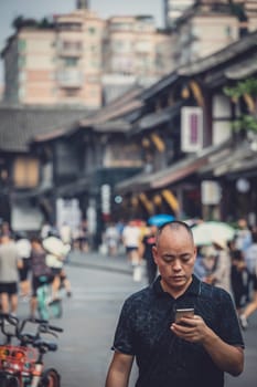 Chengdu, China -  July 2019 : Street scene in the city of Chengdu in summer, man walking and looking at the screen of his mobile phone, Sichuan Province