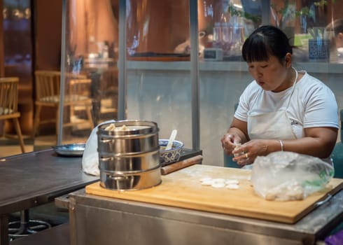 Xian, China -  August 2019 : Woman portioning flour dough in preparation for making popular baozi buns in a small local bakery on the street in Muslim Quarter