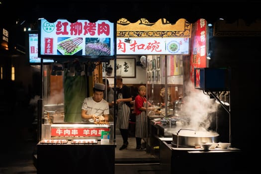 Xian, China -  August 2019 : Chef preparing hot food on a food stall operating at night on the street in the Muslim Quarter