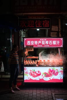 Xian, China -  August 2019 : Woman standing in front of the Fresh pomegranate juice stall operating at night on the street in the Muslim Quarter