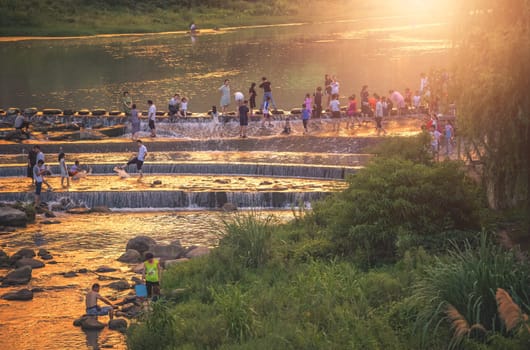 Wulingyuan, China -  August 2019 : People crossing the river during stormy sunset near Xibu Street, located near the ruins of the ancient city of Tujia